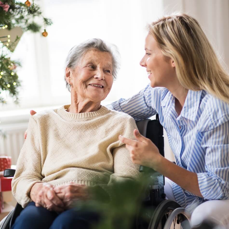 Smiling caregiver talking with senior woman in wheelchair near a window at Amazing Grace Senior Living
