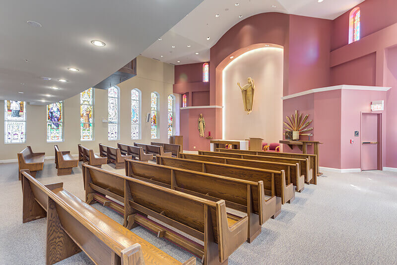 Side view of chapel with wooden pews and colorful stained-glass windows at Amazing Grace Senior Living