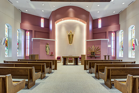 Chapel interior with wooden pews, stained glass windows, and religious statues at Amazing Grace Senior Living