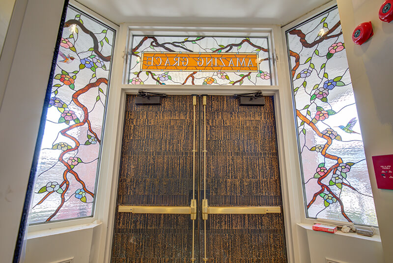 Stained glass entrance with floral and bird design reading “Amazing Grace” above the doorway