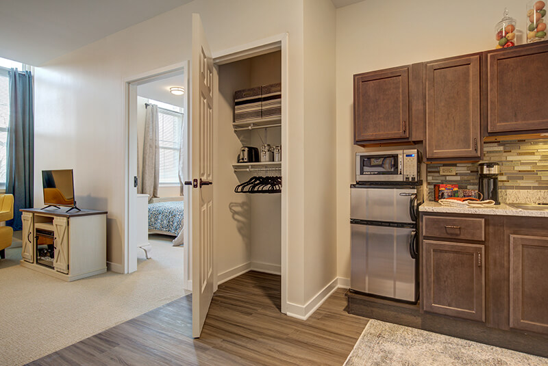Compact one-bedroom apartment kitchen with pantry storage, microwave, and stainless mini-fridge at Amazing Grace Senior Living