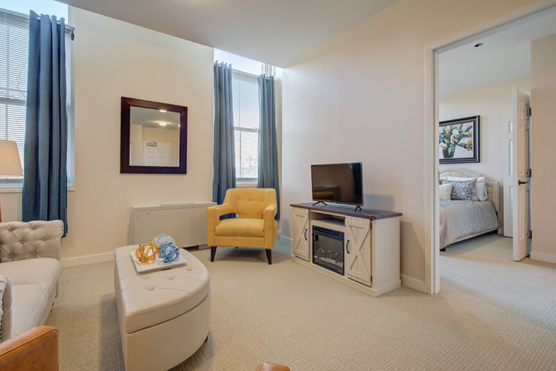 Comfortable one-bedroom apartment living room with sofa, recliner, and natural light at Amazing Grace Senior Living