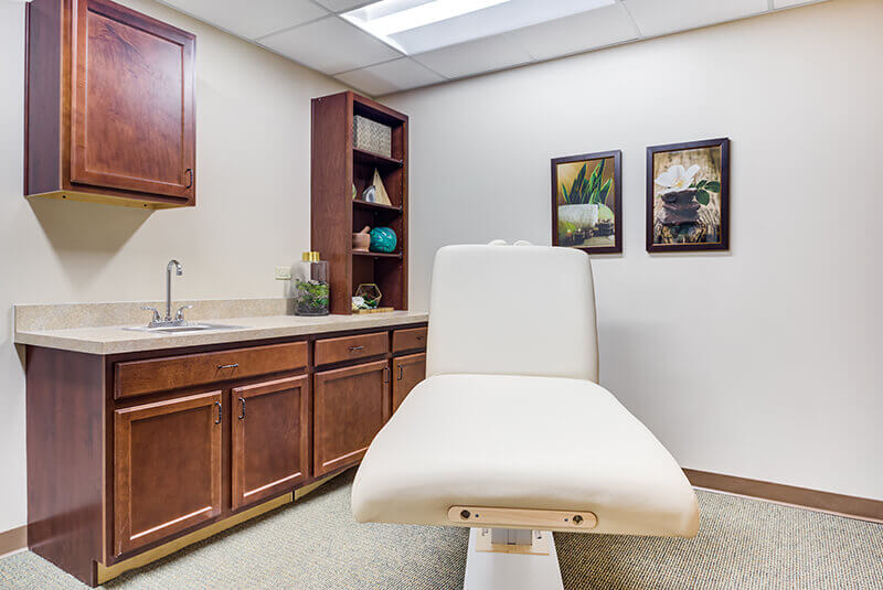 Private medical exam room with treatment chair and cabinetry at Amazing Grace Senior Living