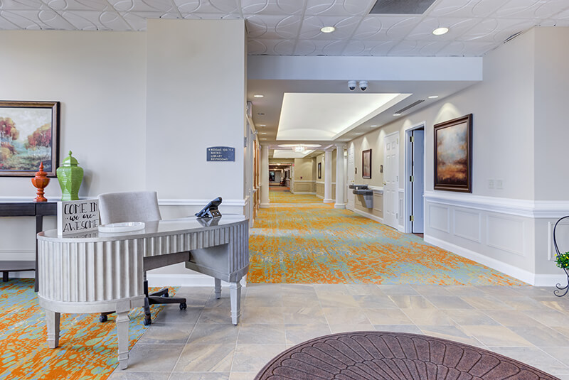 Reception desk and hallway with decorative art and warm lighting at Amazing Grace Senior Living