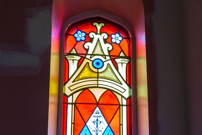 Decorative stained-glass window with red and blue designs and floral accents at Amazing Grace Senior Living