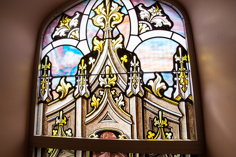 Close-up of ornate stained-glass window with decorative gold and pastel details at Amazing Grace Senior Living
