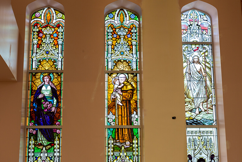Three stained-glass windows depicting religious figures at Amazing Grace Senior Living Chapel