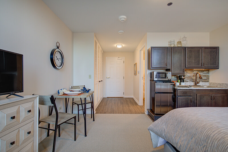Wide view of the studio apartment interior including bedroom, kitchen, and entryway at Amazing Grace Senior Living