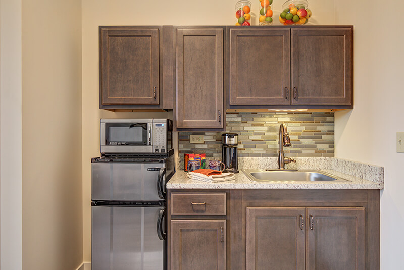 Front view of studio kitchenette with sink, microwave, and decorative backsplash at Amazing Grace Senior Living