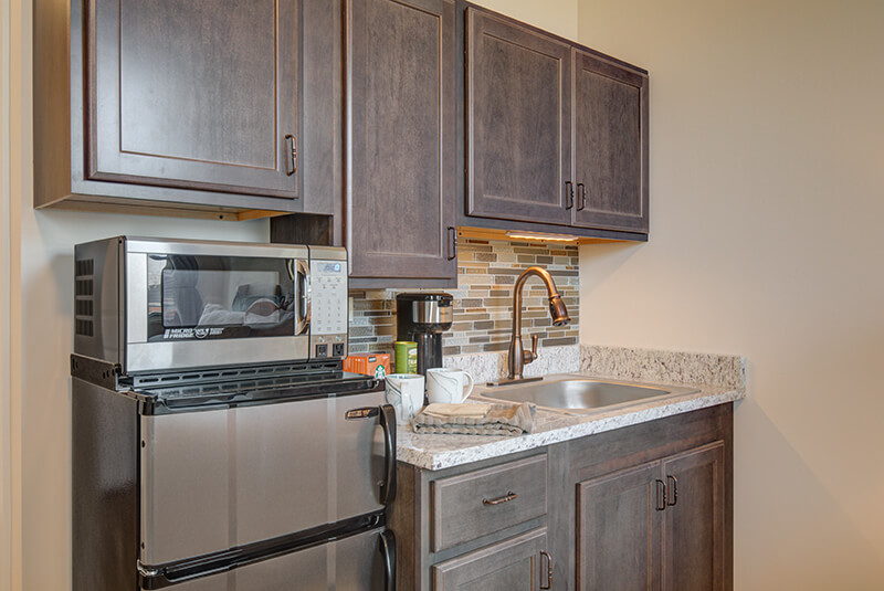 Studio kitchenette featuring granite countertop, stainless steel appliances, and modern cabinetry at Amazing Grace Senior Living