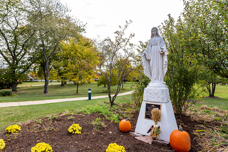 Outdoor statue surrounded by trees and seasonal flowers on the walking path at Amazing Grace Senior Living